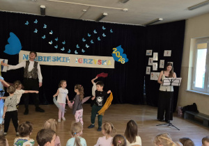 dzieci tańczą z kolorowymi chustami, obok śpiewa wokalistka