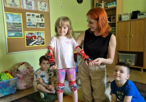 Nauczycielka i dziewczynka prezentują właściwy sposób zakładania ochraniaczy