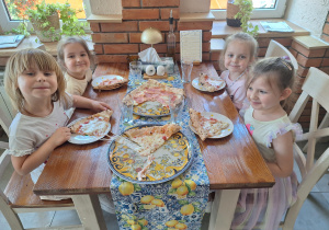 dzieci siedzą przy stole z pizzą