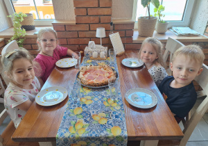 dzieci siedzą przy stole z pizzą