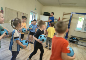 Dzieci biegają po sali gimnastycznej trzymając piłki