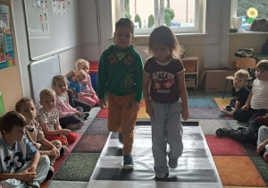 Dzieci ćwiczą przechodzenie przez jezdnię z sygnalizatorem świetlnym.