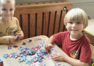 Chłopcy układają puzzle przy stolikach.