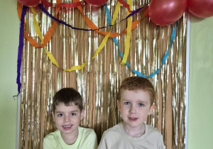 Dwóch uśmiechniętych chłopców pozuje do zdjęcia na tle dekoracji