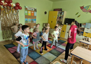 Dzieci w sali przedszkolnej tańczą układ prezentowany przez instruktorkę