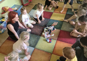 Dzieci z nauczycielką siedzą w kole na dywanie, przed nimi na środku leżą skarpetki