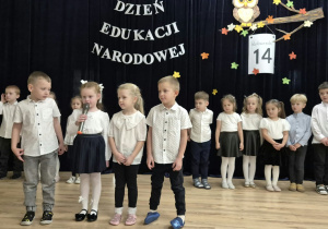 Dzieci z grupy IV stoją na scenie, jedna z dziewczynek mówi wiersz do mikrofonu